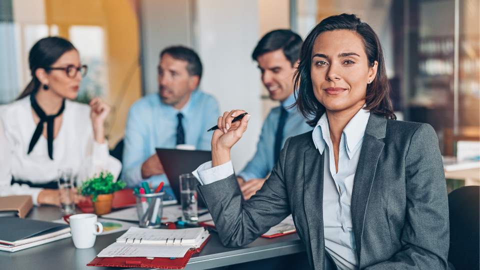 Una empresaria joven en una reunión de trabajo en primer plano con su equipo atras.