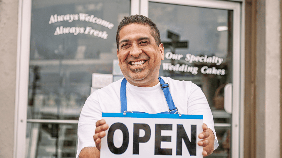 A pastry shop owner holding a sign that says "open"