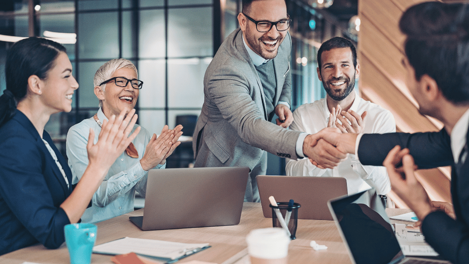 A group of employees celebrating while two men do a hand shake