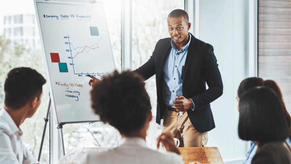 un hombre enseñando a un grupo de personas sobre la diferencia entre las ventas y los gastos de la empresa