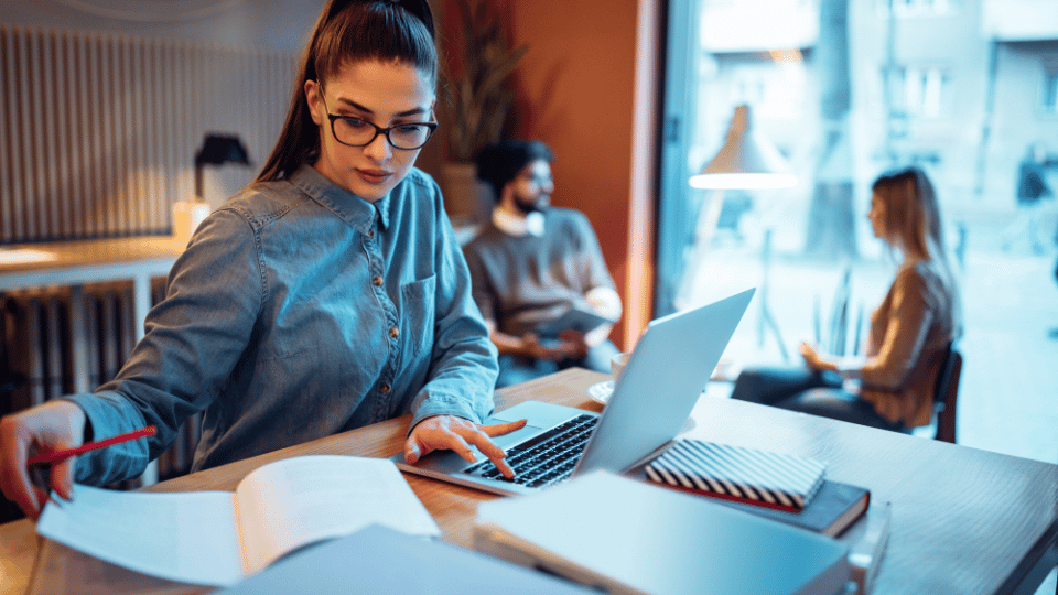 Young woman working on laptop in a busy café.