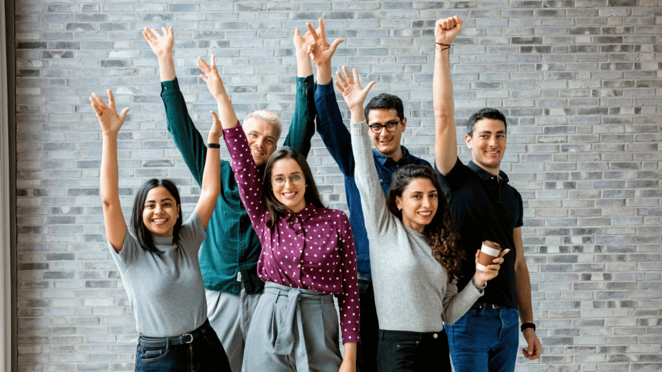 Group of young adults celebrating with arms raised