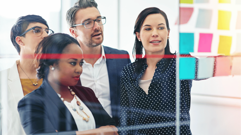 Professionals discussing ideas around a board with colorful notes.