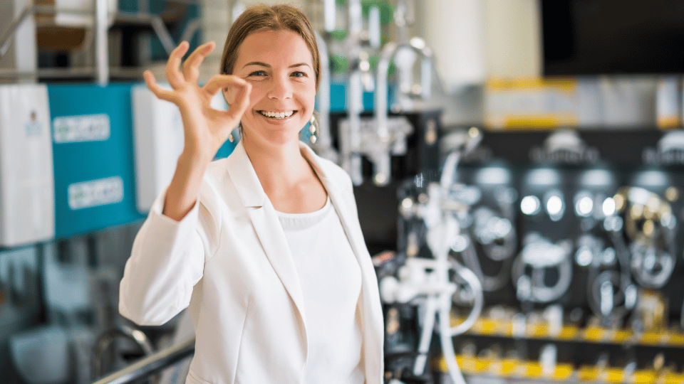 A cheerful woman making an "OK" sign in a lab setting illustrates the success of women-led businesses, possibly supported by specialized loans.