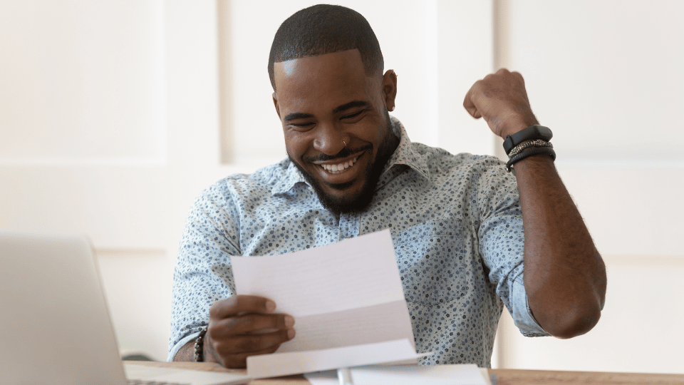 A happy man at a desk celebrates good news in a letter, possibly about a business loan.