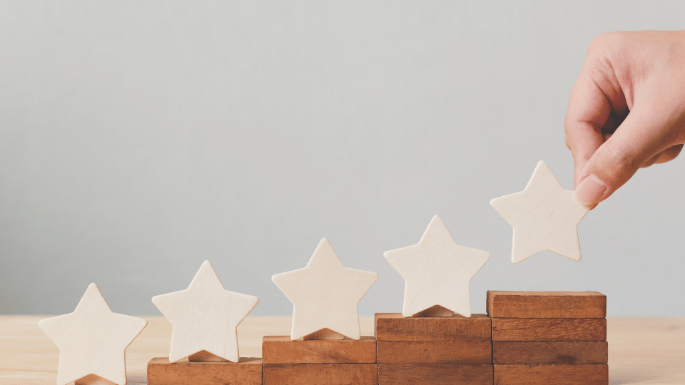 A hand placing the fifth star on a stair-like arrangement of wooden blocks, symbolizing the achievement of top customer service ratings.