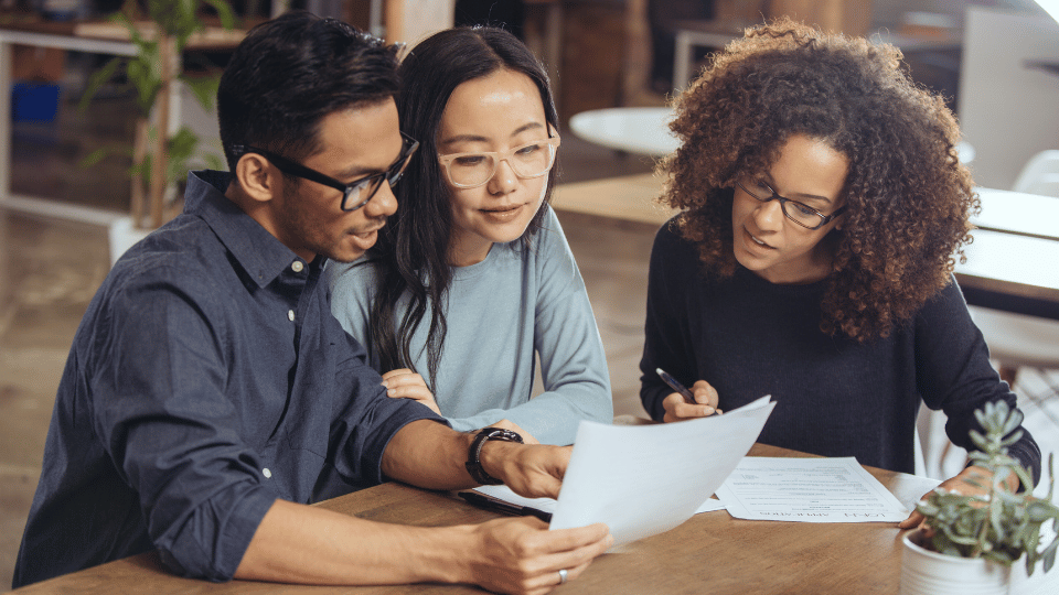 A group of three colleagues review documents together at a table, illustrating teamwork and collaboration while discussing different types of business ownership.